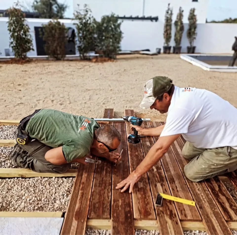 Two gardeners fastening a timber deck over gravel